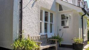 A house with a white exterior, a front door, a bench, and potted plants. - Warren Cottage (Dartmouth)