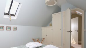 A bedroom with a bed, a wardrobe, a hanging rack, and a window. - Warren Cottage (Dartmouth)