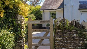 A wooden gate leading to a house with a stone wall and greenery on the left. - Warren Cottage (Dartmouth)