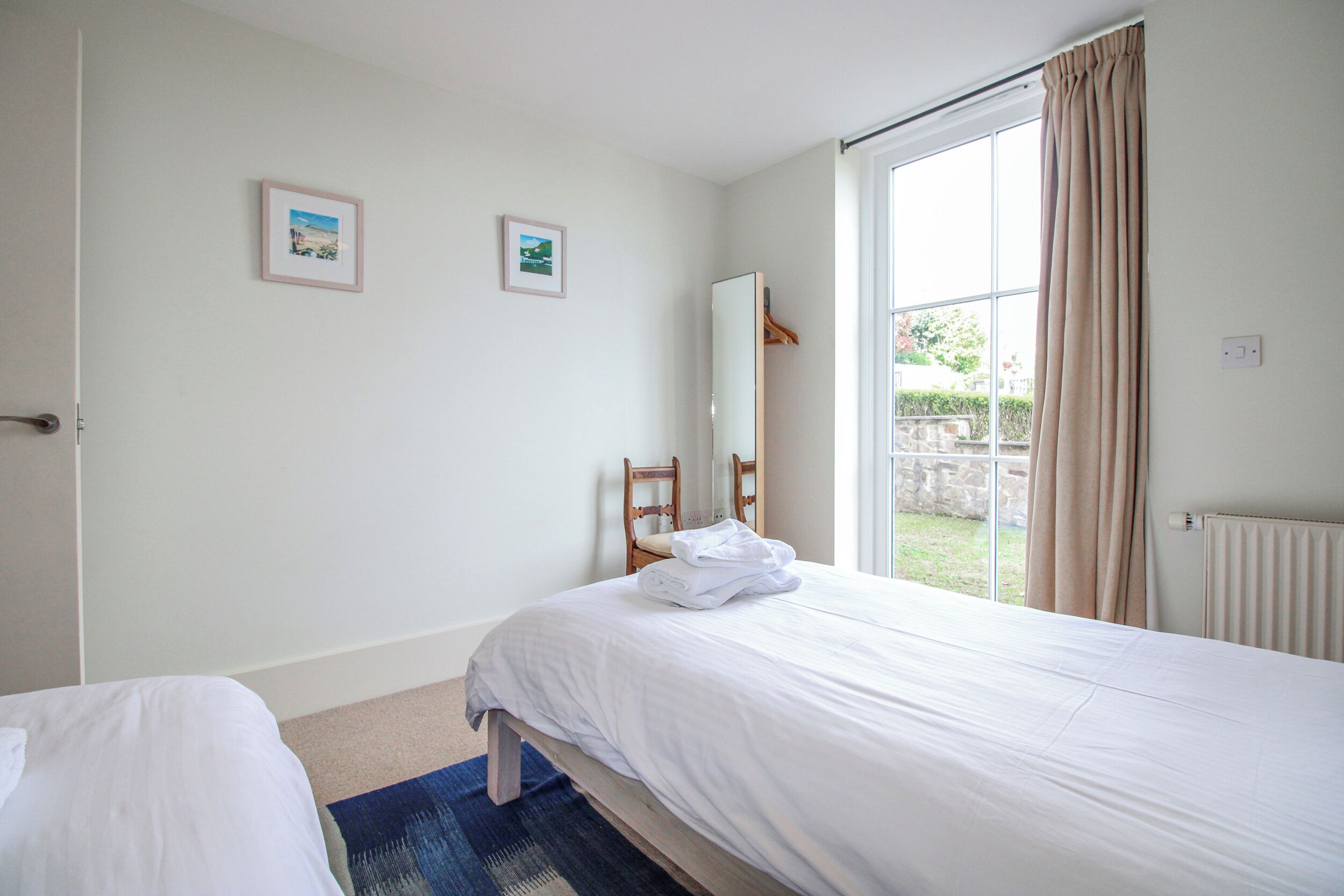 A bedroom with a bed, a chair, a window with curtains, and two framed pictures on the wall.