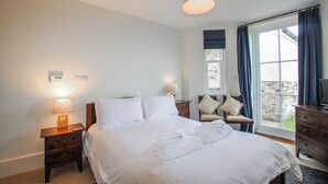 Una habitación de hotel con cama, lámparas de noche, una silla, cómoda y ventana con cortinas.