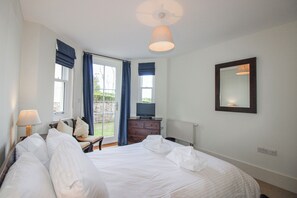 Ein Hotelzimmer mit Bett, Schminktisch, Fernseher, einem fenster mit Vorhängen und einem Spiegel an der Wand.