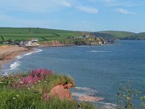 Un paisaje costero con una playa, casas y colinas al fondo.
