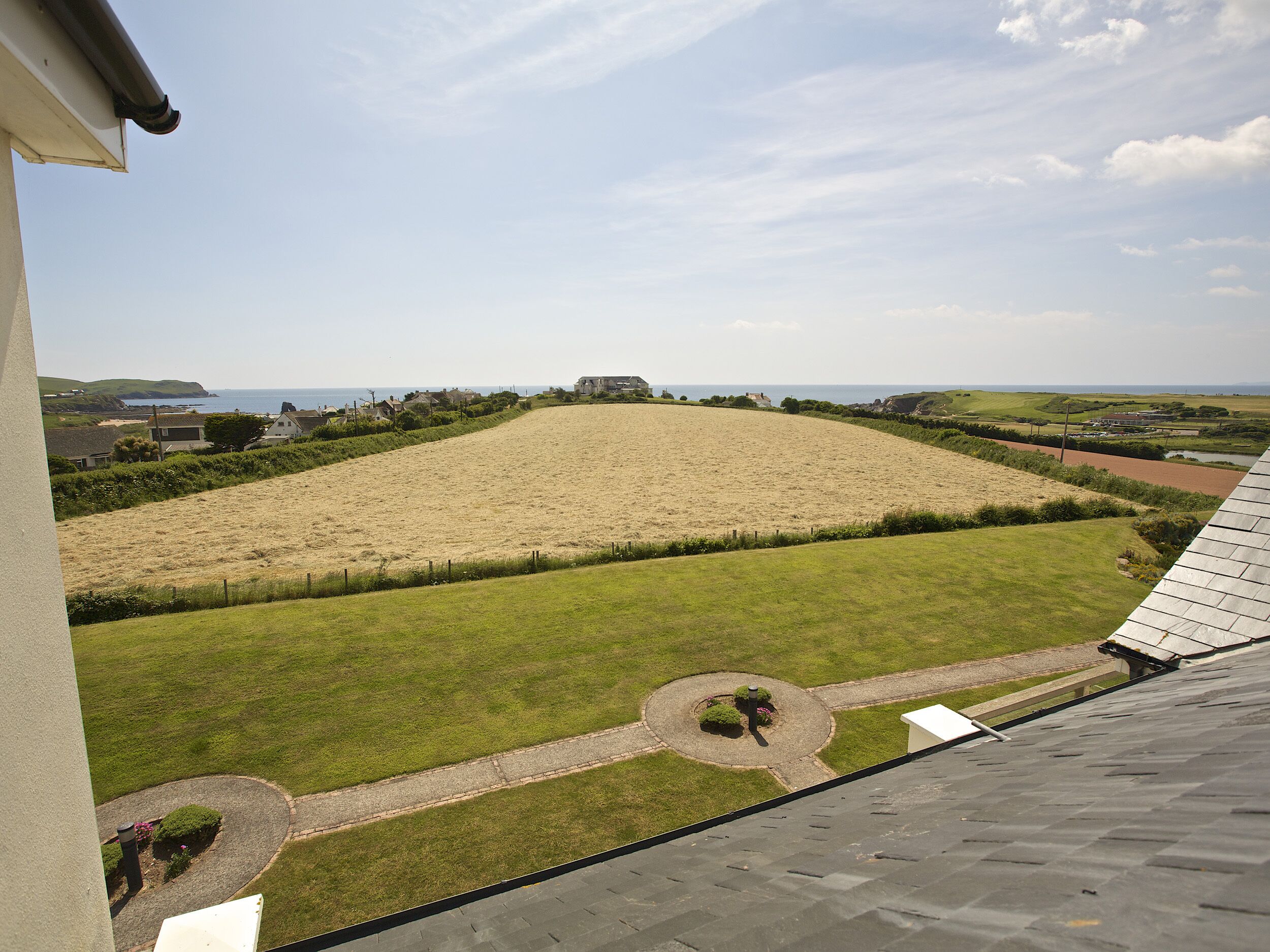 Vista desde una ventana sobre un campo cubierto de hierba, con un pequeño jardín circular y un edificio lejano.