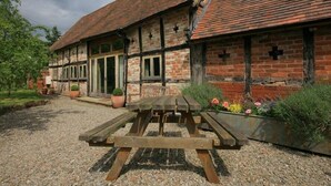 A traditional half-timbered house with a gravel driveway and a wooden picnic table in front. - Whites Farm Barn (Dymock)