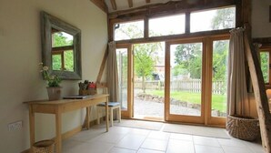A room with a wooden table, a chair, a potted plant, and a large sliding glass door leading to an outdoor area. - Whites Farm Barn (Dymock)