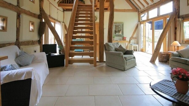 A spacious living room with a high wooden ceiling, a staircase, and a large window. - Whites Farm Barn (Dymock)