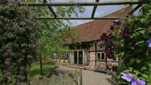 A rustic stone building with a tiled roof, a gravel pathway, and a wooden fence. - Whites Farm Barn (Dymock)