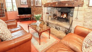 A cozy living room with leather sofas, a glass coffee table, a fireplace, and a television. - Hadcroft Cottage (Moreton-in-Marsh)