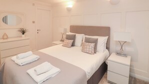 A neatly arranged bedroom with a large bed, bedside tables, a mirror, and a small plant. - 1 The Old Coach House (Dartmouth)