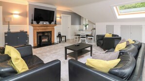 A modern living room with a fireplace, a flat-screen TV, and a dining area with a table and chairs. - 1 The Old Coach House (Dartmouth)