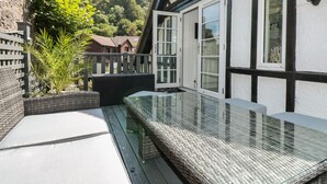 A balcony with a glass balustrade, a wicker bench, and a view of a residential area with houses and trees. - 1 The Old Coach House (Dartmouth)