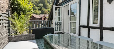 A balcony with a glass balustrade, a wicker bench, and a view of a residential area with houses and trees.