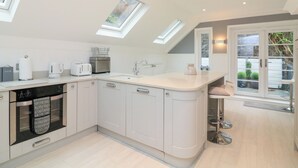 A modern kitchen with white cabinetry, a built-in oven, and a large island with a sink. There are skylights providing natural light. - 1 The Old Coach House (Dartmouth)