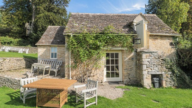 A stone cottage with a thatched roof, a small garden, and a wooden bench. - Mayfly Cottage (Cirencester)