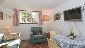 A cozy living room with a sofa, armchair, and a table with a bottle and glasses. - Mayfly Cottage (Cirencester)
