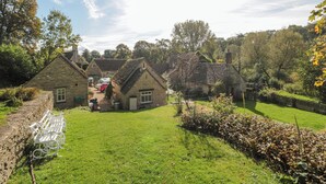 A traditional stone cottage with a well-maintained garden and a pathway leading to the entrance. - Mayfly Cottage (Cirencester)