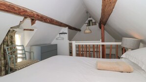 A bedroom with a sloped ceiling, a bed, a desk, and a chair. - Mayfly Cottage (Cirencester)
