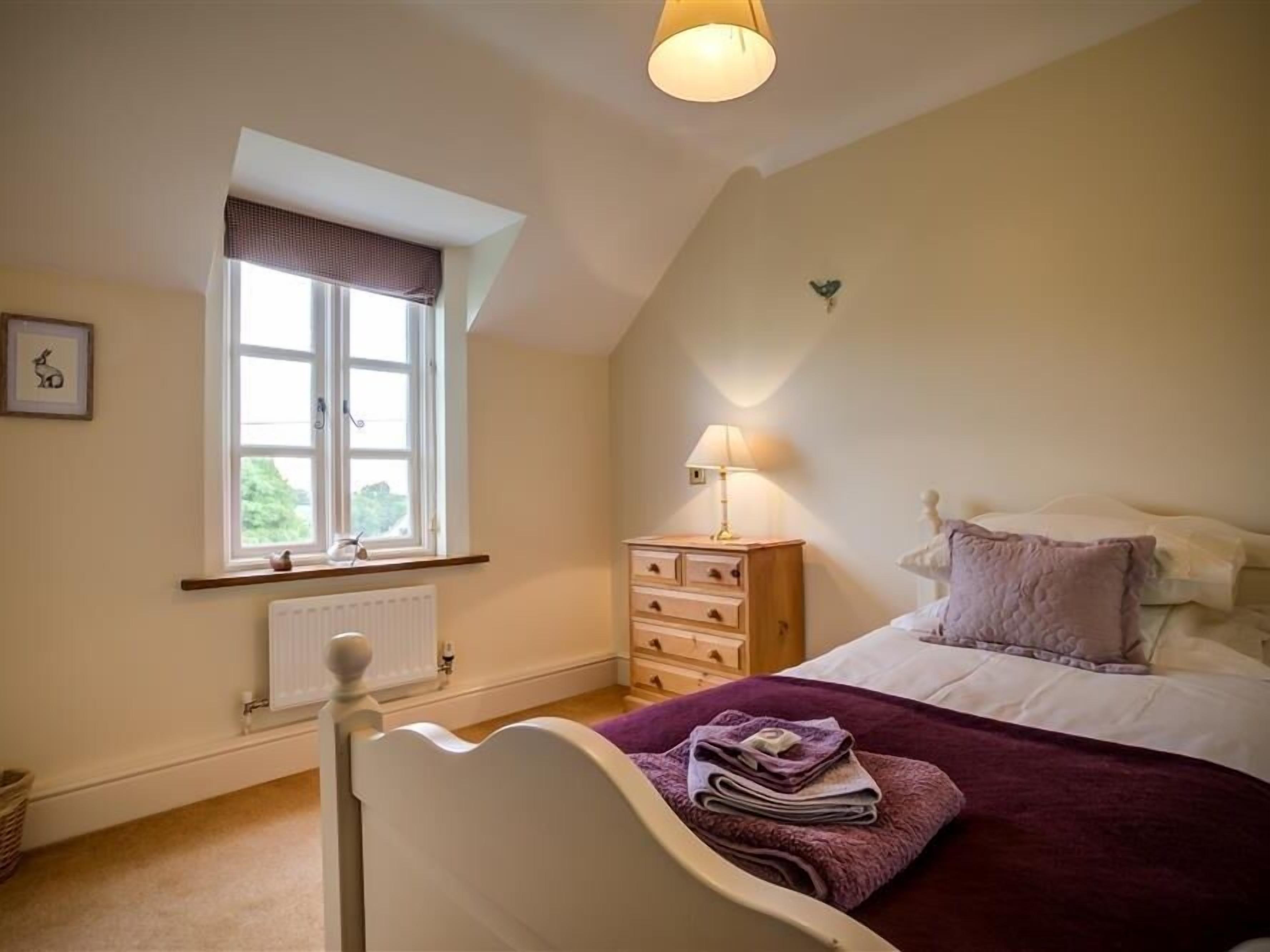 A bedroom with a bed, a nightstand, a window, and a radiator.