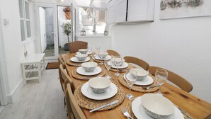 A dining area with a wooden table set for six, white walls, and a view into the adjacent room. - Waverley House (Beaumaris)