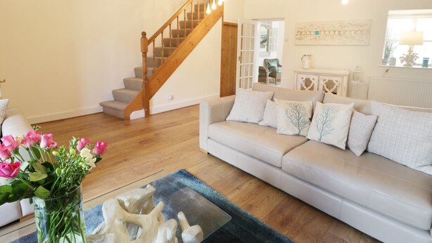 A living room with a wooden staircase, a white sofa, and a vase of flowers. - Waverley House (Beaumaris)