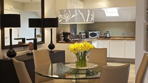 A modern kitchen with white cabinets, a microwave, and a coffee maker. There is a dining area with a glass table and chairs, and a vase with yellow flowers. - Diddly Squat, 43 Dart Marina (Dartmouth)