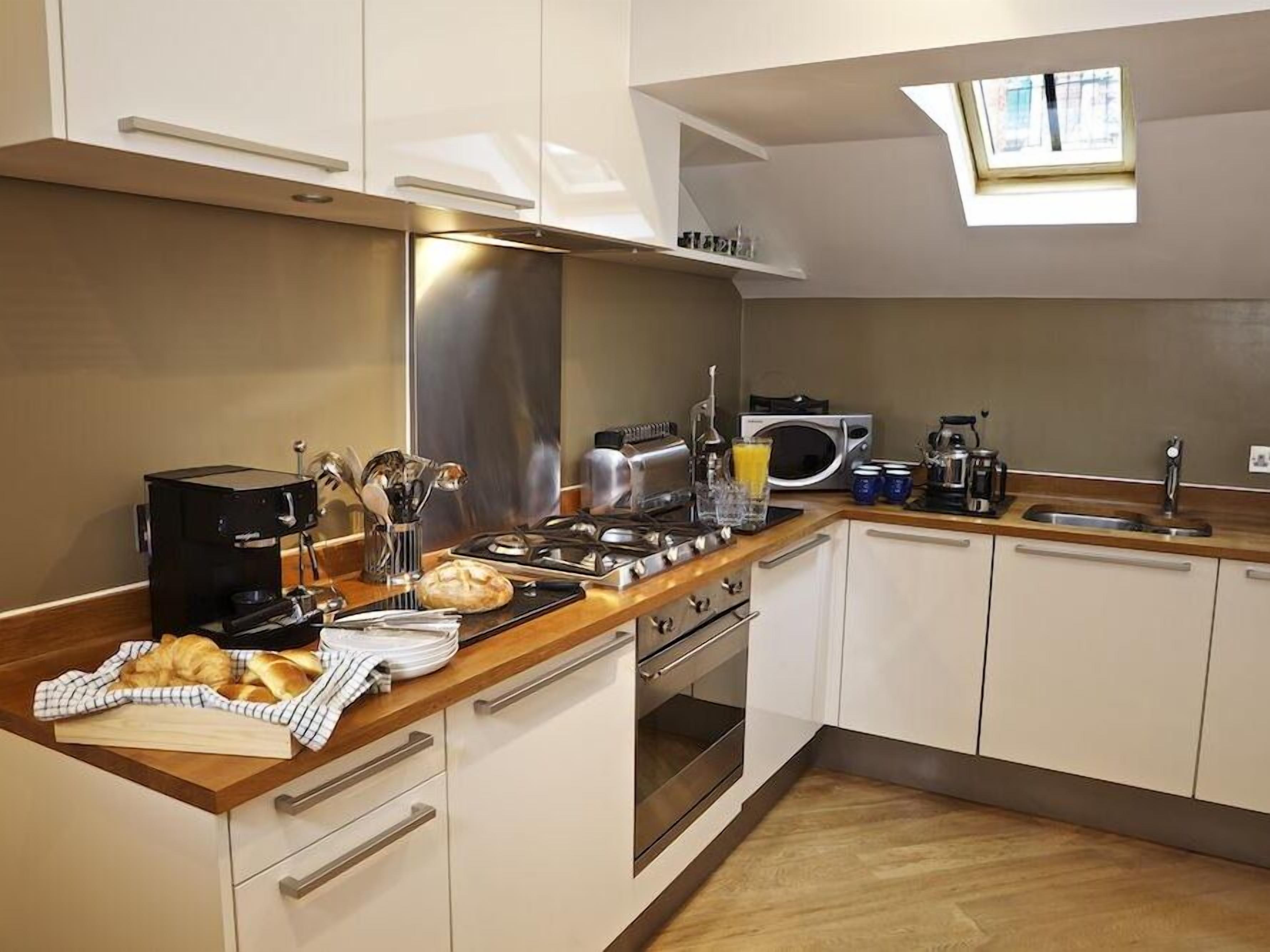 A modern kitchen with white cabinets, a wooden countertop, a built-in oven, a microwave, and a coffee machine.