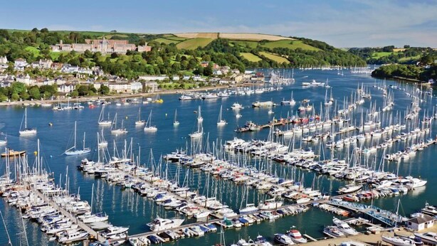 A marina filled with numerous boats, surrounded by a town with historic buildings and green hills in the background. - Diddly Squat, 43 Dart Marina (Dartmouth)