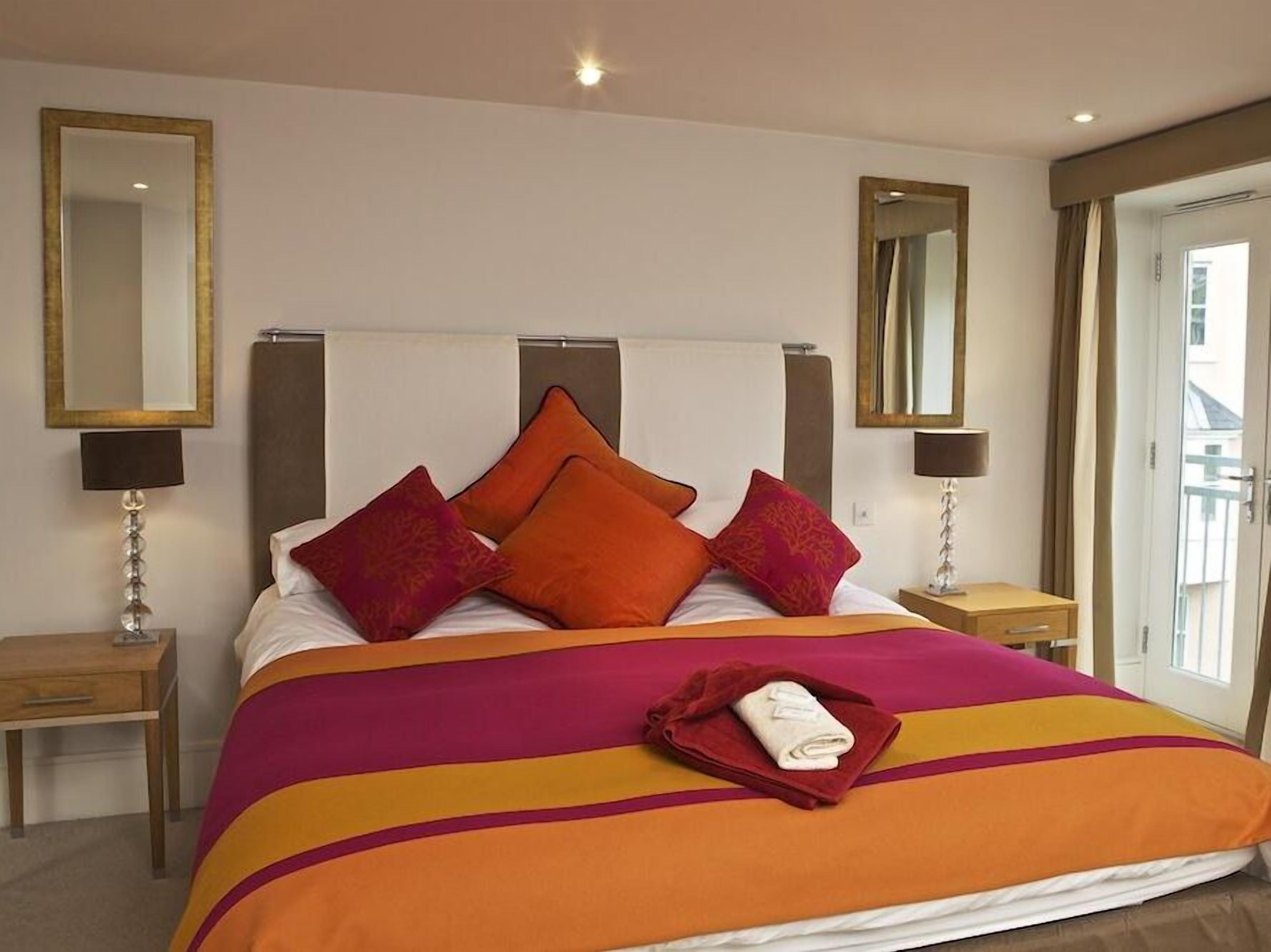 A hotel room with a large bed, multiple pillows, two bedside tables with lamps, and a large mirror on the wall.