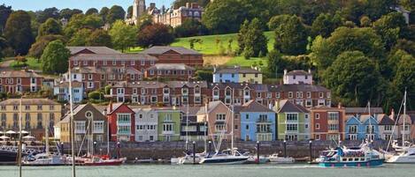 A coastal town with colorful houses, a marina with boats, and a historic building on a hill.