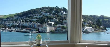 A table with a bottle and glasses, overlooking a harbor with boats and a hillside of buildings.