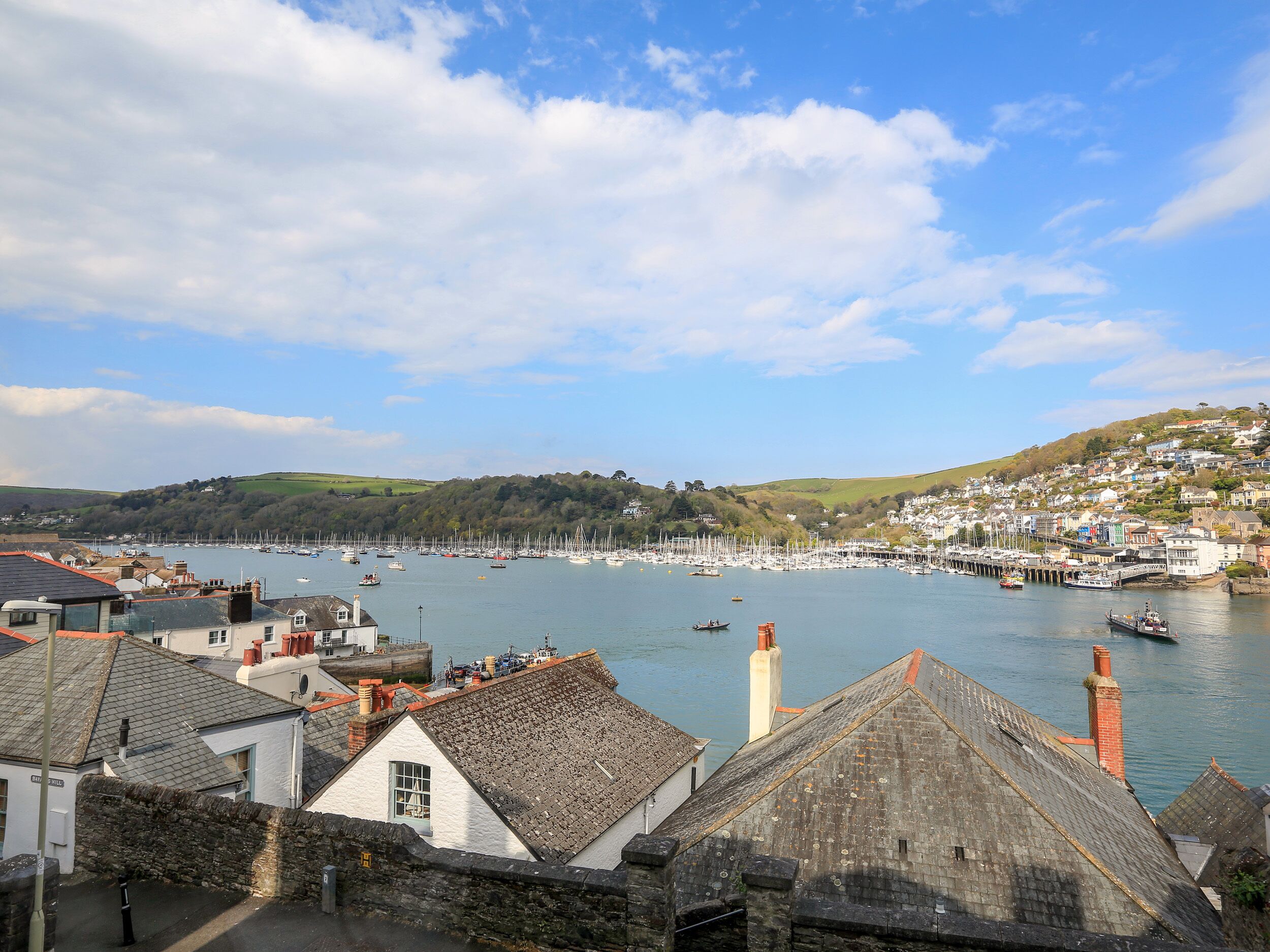 A coastal town with historic buildings, a marina with boats, and a hilly backdrop.