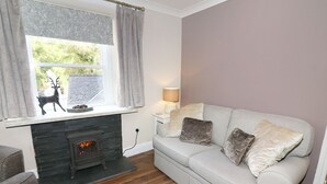 A cozy living room with a fireplace, a sofa with cushions, a lamp, and a window with curtains. - Shepherd's Crook (Ambleside)