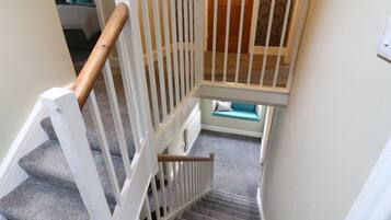 Una escalera con barandillas blancas y un pasamanos de madera, que lleva a un rellano con un banco azul.