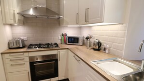 A modern kitchen with white cabinets, a stainless steel range hood, a built-in oven, a microwave, and a sink. - Shepherd's Crook (Ambleside)