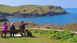 Trois personnes sont assises sur un banc, d’où elles peuvent admirer un paysage côtier composé de collines et d’une étendue d’eau.