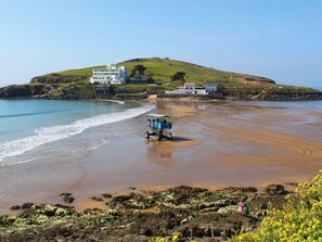 A coastal area with a beach, a hill with buildings, and a vehicle on the sand. - Homefield House (Kingsbridge)