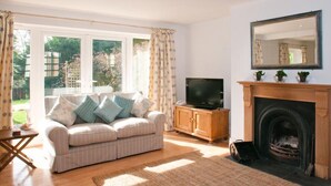 A living room with a sofa, television, fireplace, and large windows. - Homefield House (Kingsbridge)