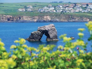 Un paysage côtier avec une formation rocheuse imposante au premier plan et un village en arrière-plan.