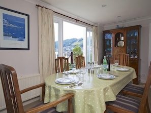A dining area with a table set for four, chairs, a cabinet with glass doors, and a framed picture on the wall.