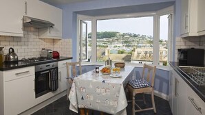 A kitchen with a dining table set for breakfast, a view of the town, and a large window.