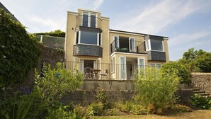 A modern two-story house with a balcony, a small patio, and a stone wall.