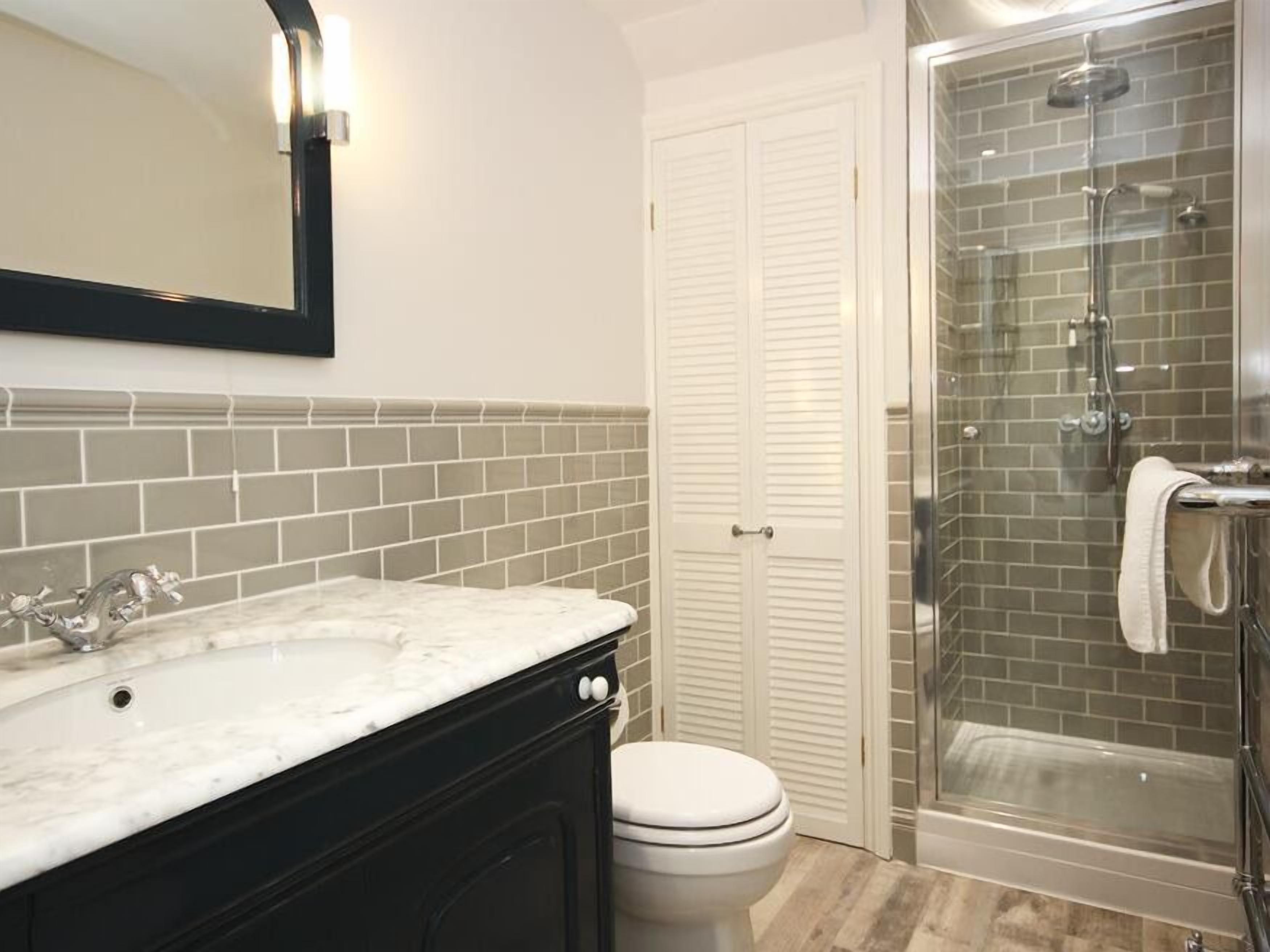 Un bagno con lavabo in marmo, un water, box doccia in vetro e una porta bianca.