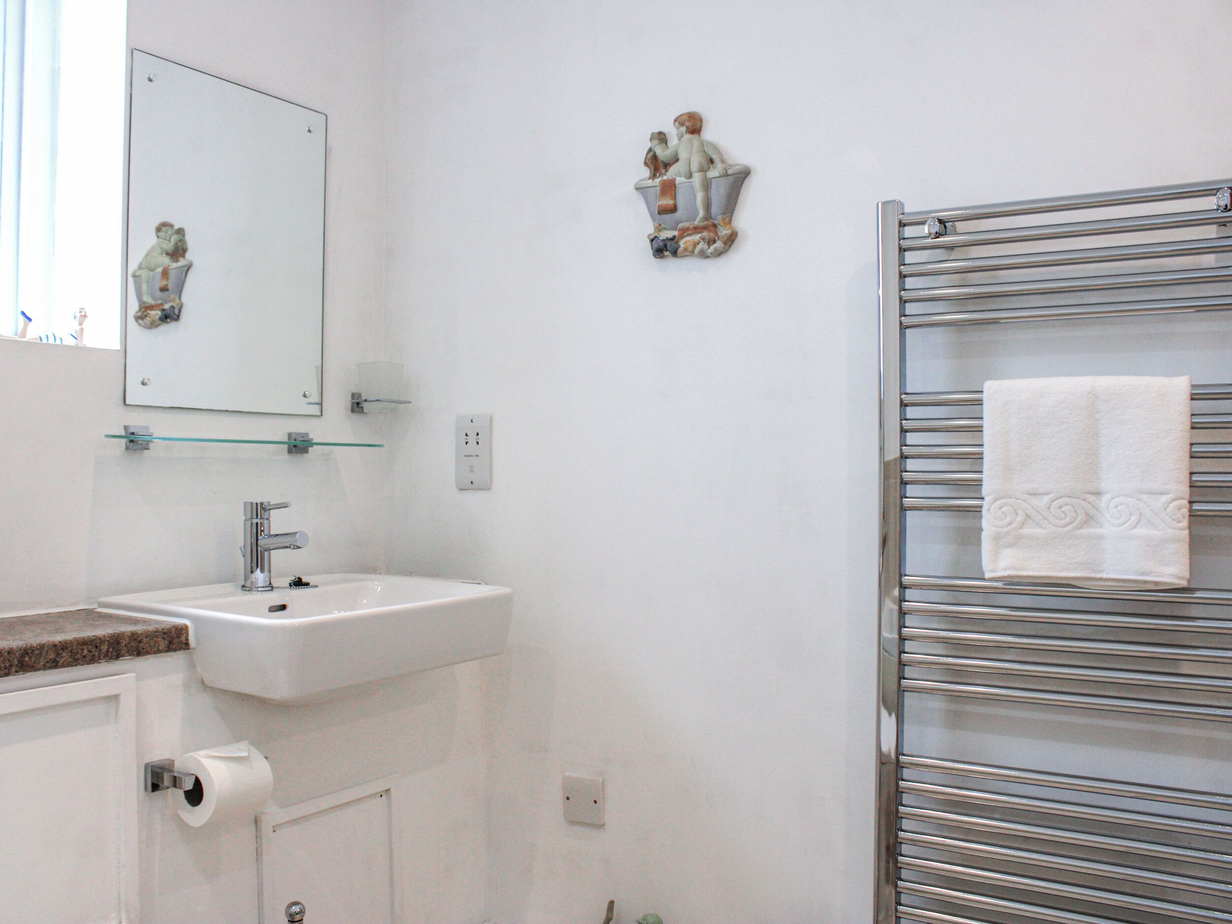 A bathroom with a white sink, a mirror, a towel rack with a folded towel, and a small decorative item on the wall.