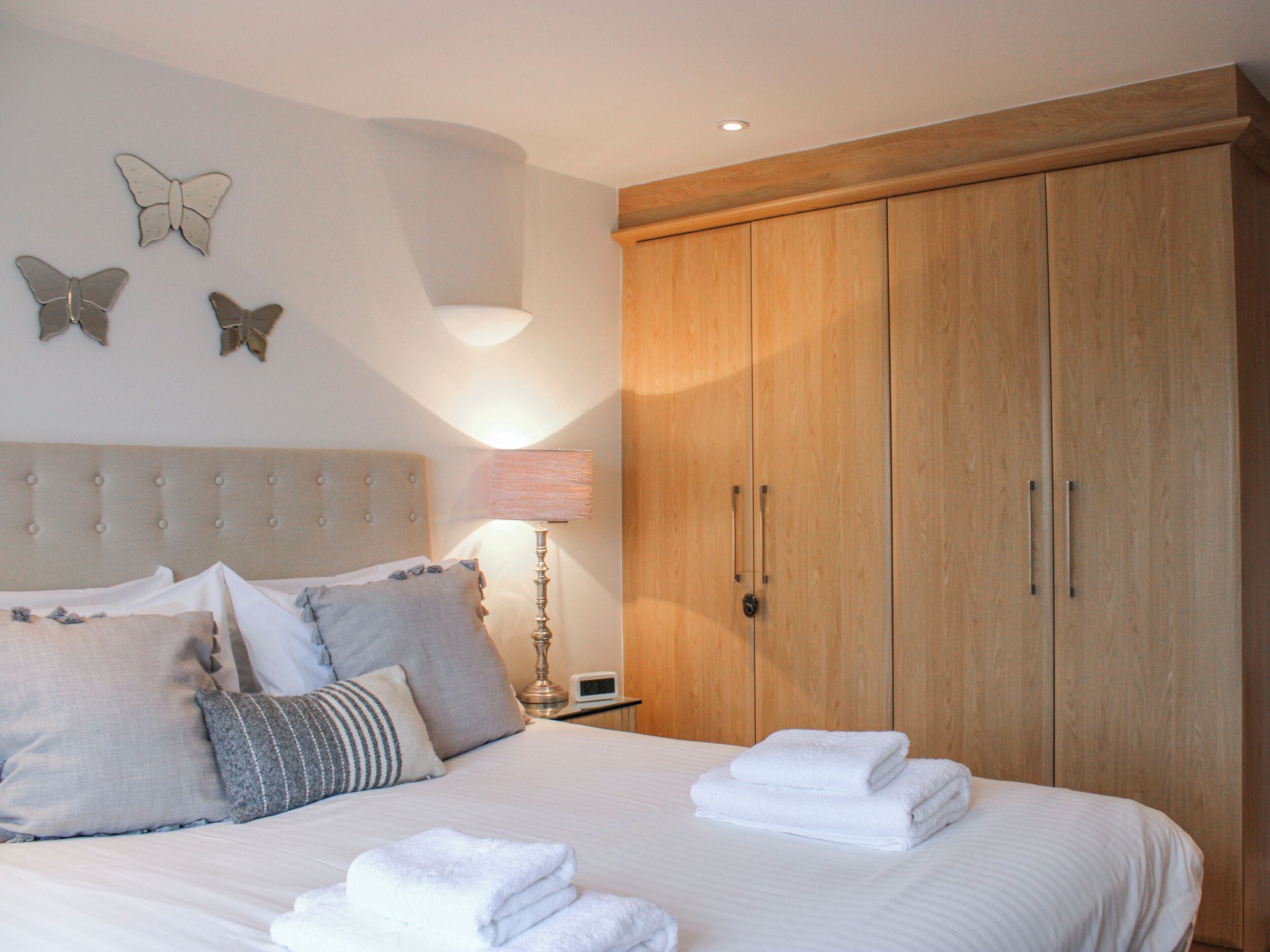 A bedroom with a large bed, a wooden wardrobe, a bedside lamp, and butterfly wall art.