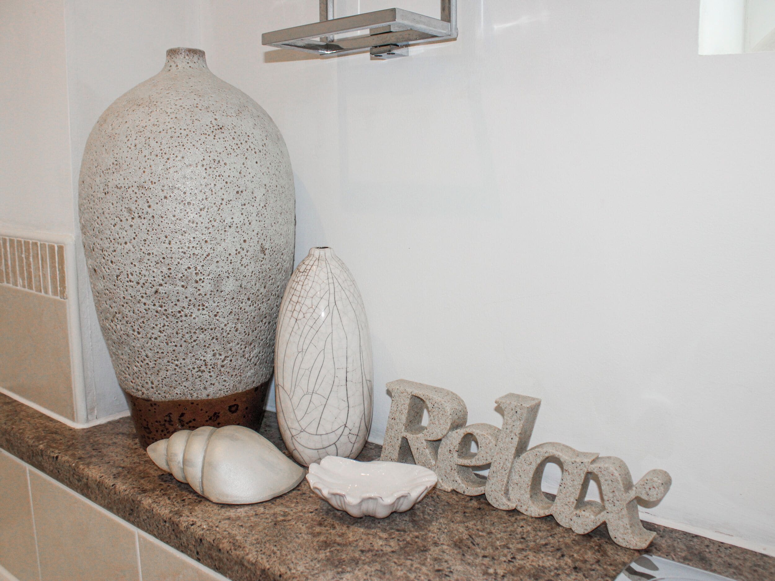 Une salle de bain avec un grand vase à motifs, un vase plus petit et une pancarte «Détendez-vous» sur un comptoir carrelé.