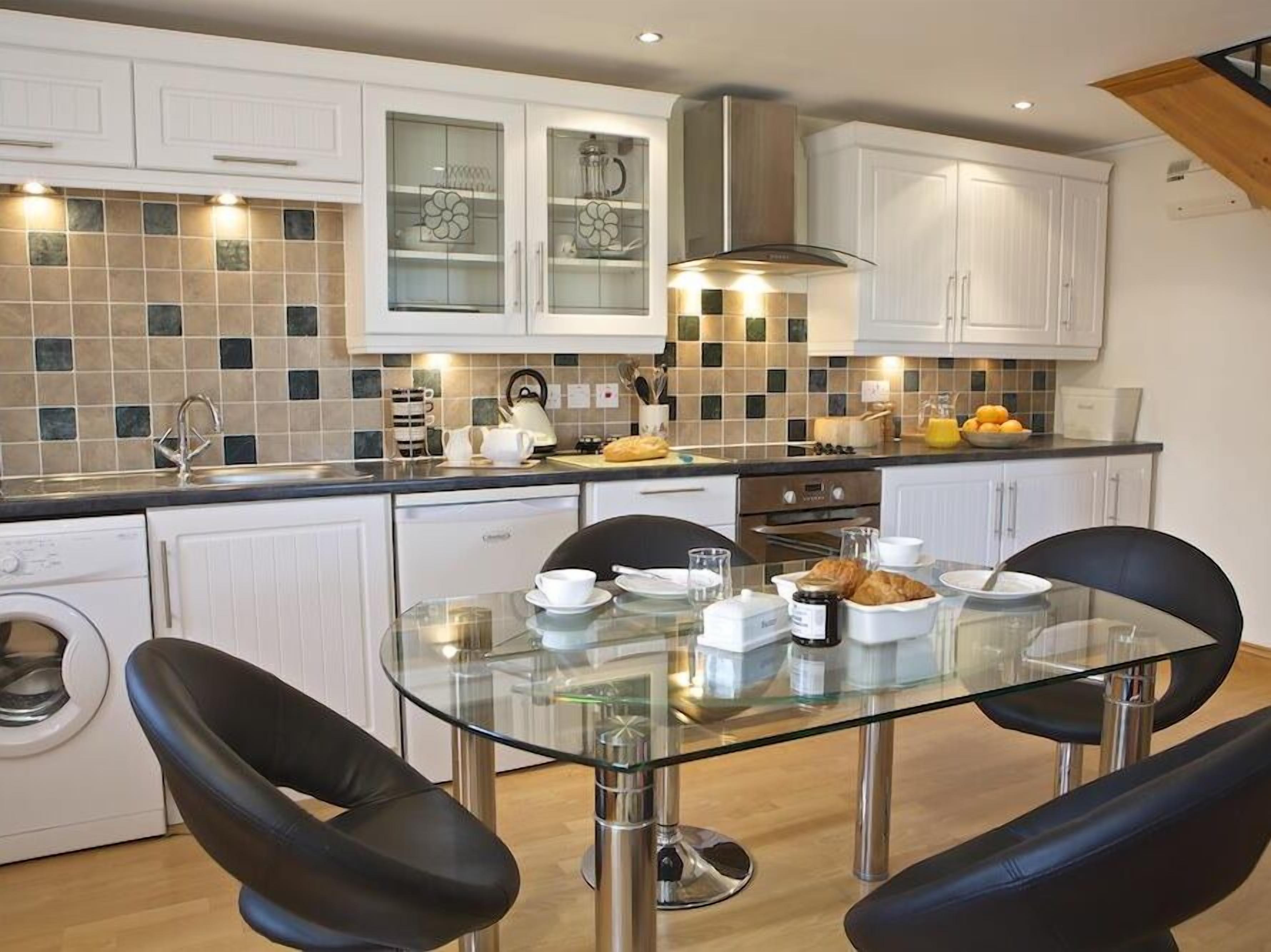 A modern kitchen with white cabinets, a glass-top dining table, and a built-in oven.