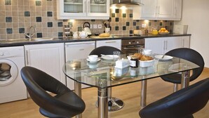 Eine moderne Küche mit weißen Schränken, einem Esstisch mit Glasplatte und einem eingebauten Backofen.