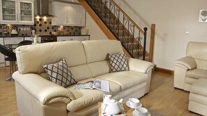 Ein Wohnzimmer mit einem beige gefärbten Sofa, einem Holztisch mit Teeservice und einer Treppe mit schmiedeeisernem Geländer.