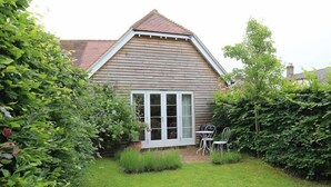 Une maison en bois avec un toit à pignon, une porte blanche et une petite terrasse avec une table et des chaises.